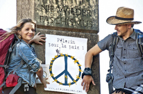 Zwei Pilger mit Friedensplakat vor Kriegsdenkmal