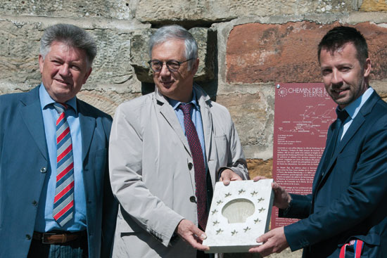 Drei Männer vor Kirchenmauer präsentieren eine Steintafel