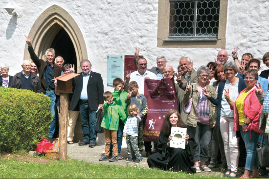 Gruppe vor Kirche feiert Muschelsteinsetzung