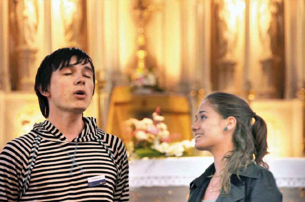 Junge Frau in Kirche schaut zu jungem Mann mit geschlossenen Augen