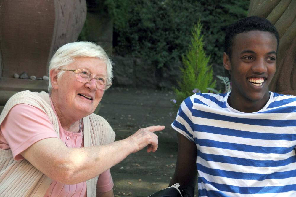 Ältere Dame zeigt im Gespräch auf lächelnden Jugendlichem