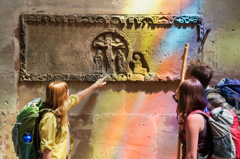 Pilgerin zeigt auf Steinbild an einer Kirchenwand