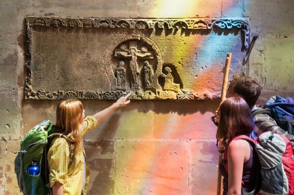 Pilgerin zeigt auf Steinbild an einer Kirchenwand