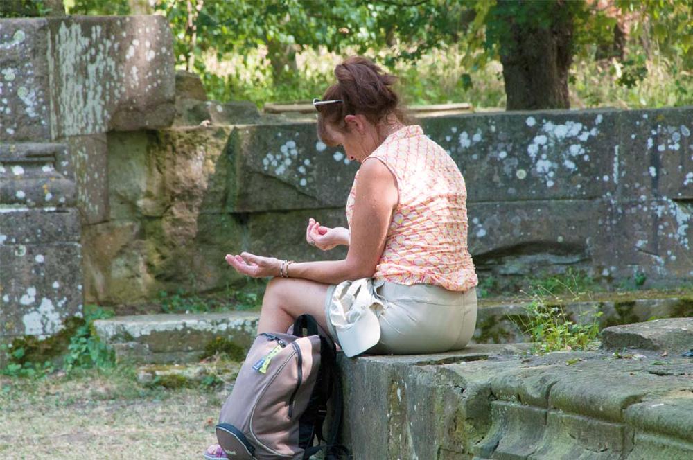 Frau sitzt in Meditationspose auf Steinmauer